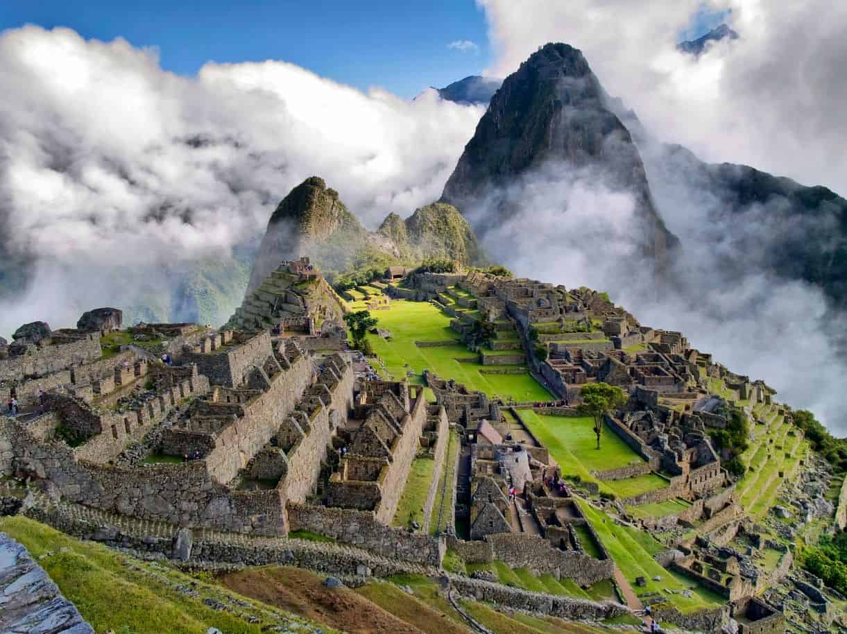 Machu Picchu's stone terraces in sunlight with clouds around the peaks behind
